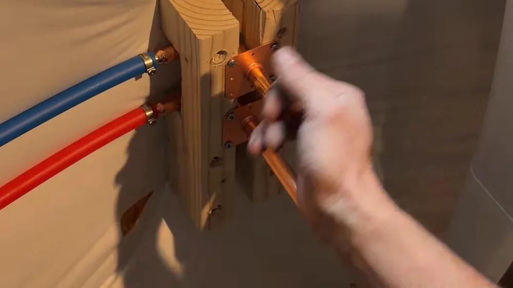 Red and blue PEX lines connected to copper fittings on a wooden block, with a hand adjusting one fitting