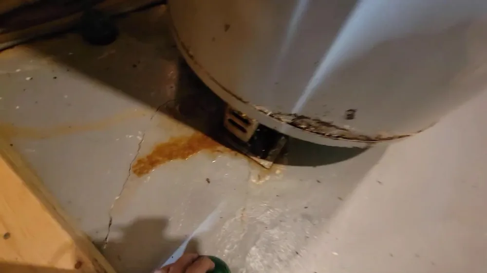 Orange rust stain on a cracked concrete floor beside the base of an old tank water heater