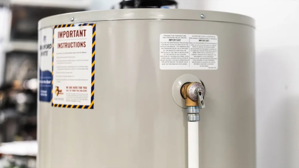 Brass temperature and pressure relief valve on the side of a tank water heater with a white discharge pipe running down