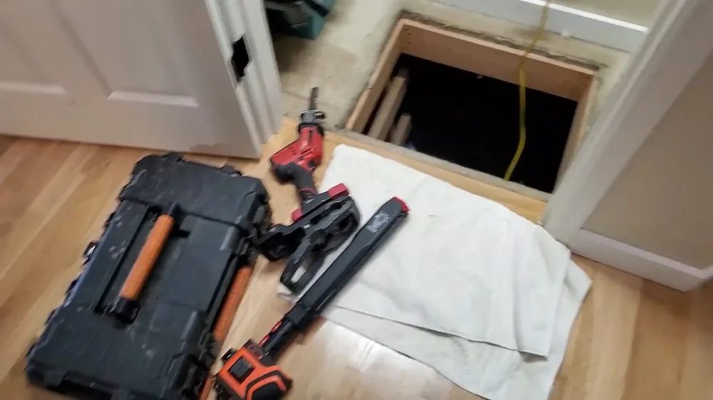 Toolbox and hand tools laid out beside an open floor access hatch on a wood floor