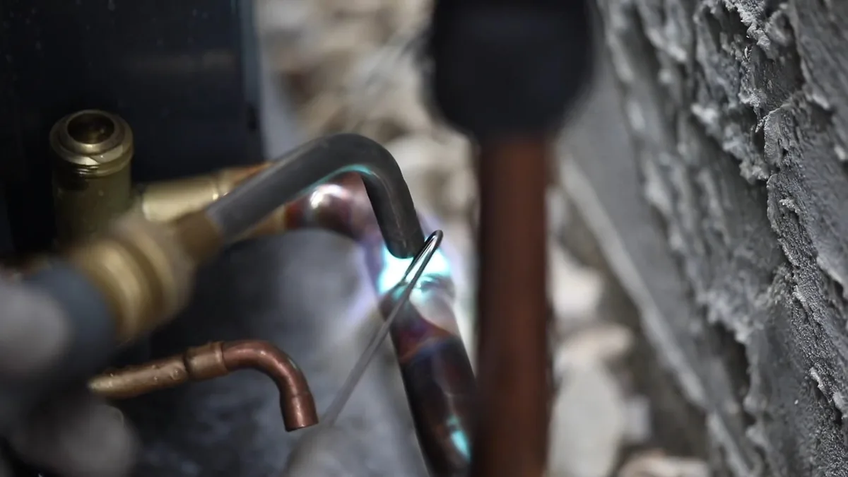 Torch flame heating a copper fitting against a rough wall while a pipe is soldered in place